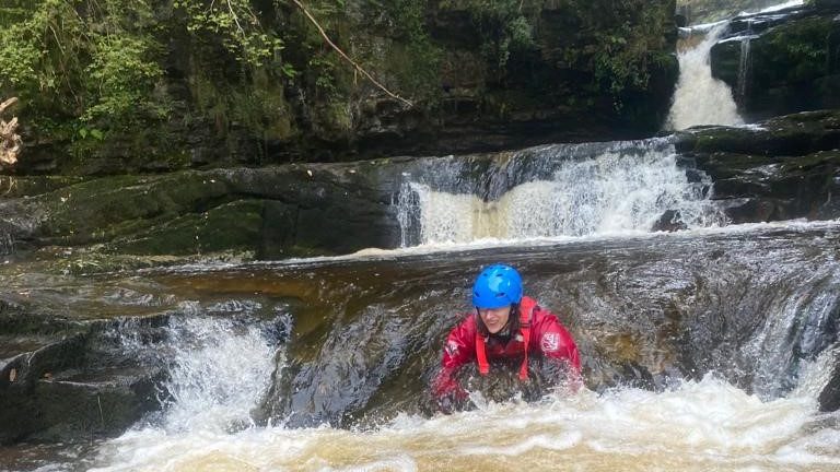 Gorge walking adventure. A person swimming down a small drop in a river.